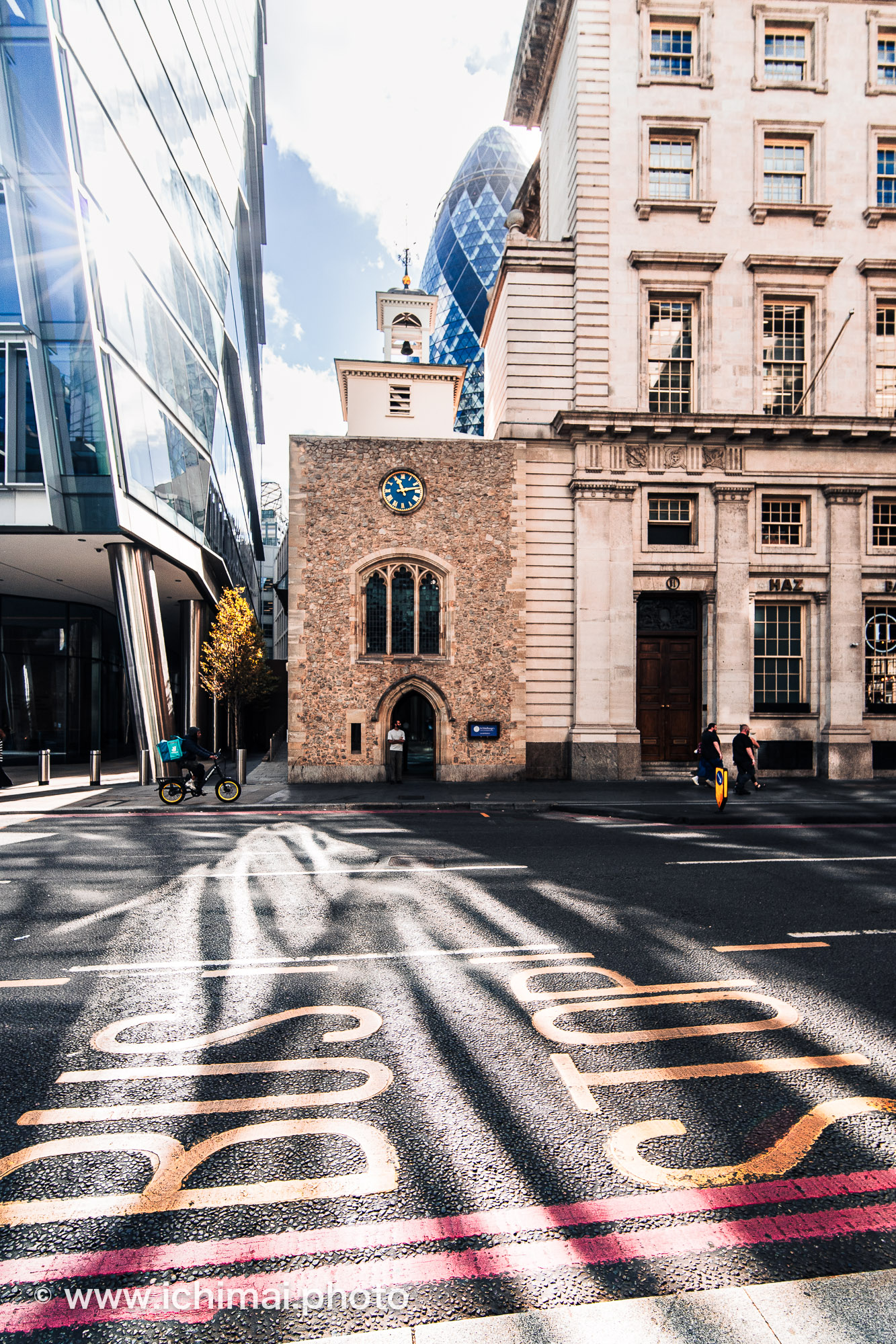 Église gothique et Gherkin dans la City de Londres, derrière une chaussée marquée BUS STOP et traversée de lumière